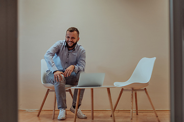 Image showing A confident businessman sitting and using laptop with a determined expression, while a beige background enhances the professional atmosphere, showcasing his productivity and expertise.