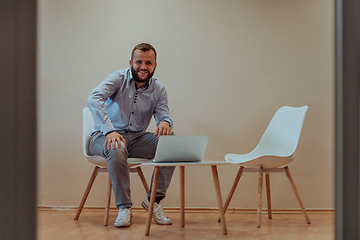 Image showing A confident businessman sitting and using laptop with a determined expression, while a beige background enhances the professional atmosphere, showcasing his productivity and expertise.