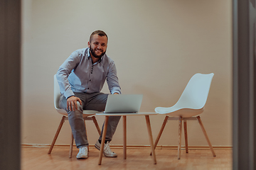 Image showing A confident businessman sitting and using laptop with a determined expression, while a beige background enhances the professional atmosphere, showcasing his productivity and expertise.