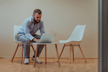 Image showing A confident businessman sitting and using laptop with a determined expression, while a beige background enhances the professional atmosphere, showcasing his productivity and expertise.