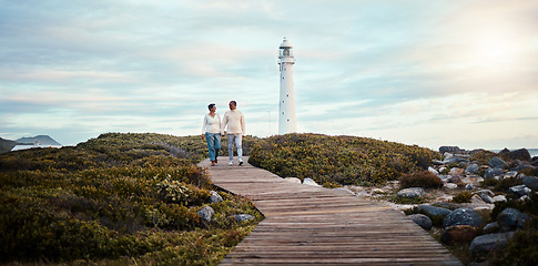 Image showing Romance, love and a couple holding hands while walking on the beach with a lighthouse in the background. Nature, view or blue sky mockup with a man and woman taking a romantic walk outside together