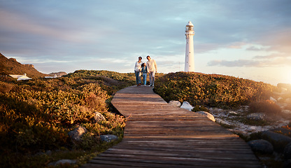 Image showing Lighthouse, family walking and nature adventure on a summer holiday at sunset by the sea. Ocean, beach walk and outdoor with a mom, father and child together with love and parents support at dusk