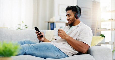 Image showing Coffee, phone and happy man on sofa with headphones for social media, video streaming service and networking mobile app. Indian person relaxing on couch in his apartment on audio tech and smartphone