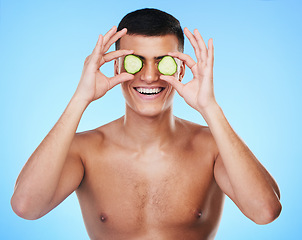 Image showing Man, beauty and cucumber over eyes with skin, grooming for hygiene and clean on blue background. Cosmetics product, natural and eco friendly skincare treatment with vegetable and self care in studio