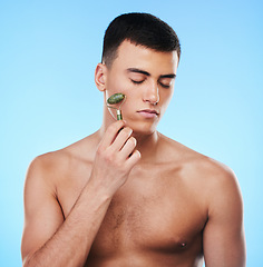 Image showing Man, beauty and face with skin, roller for skincare and grooming with hygiene on blue background. Jade crystal, model and dermatology, cosmetic tools and treatment with facial massage in a studio