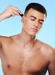 Image showing Man, skincare serum and drop in studio with beauty, wellness and facial change by blue background. Young model, oil or hyaluronic acid for glow, shine and cleaning face with cosmetic transformation