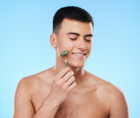 Image showing Man, beauty and face with skincare, roller for skin and grooming with smile on blue background. Jade crystal, model and dermatology, cosmetic tools and treatment with facial massage in a studio