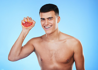 Image showing Smile, grapefruit and squeeze with portrait of man in studio for health, detox or natural cosmetics. Vitamin c, nutrition and skincare with person and fruit on blue background for self care and glow