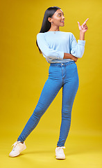 Image showing Pointing, marketing and young woman in a studio for advertising, creative or promotion. Smile, happy and full length of Indian female model with a direction hand gesture isolated by yellow background