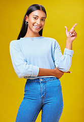 Image showing Pointing, mockup and portrait of a woman in a studio for advertising, marketing or promotion. Smile, happy and young Indian female model with a direction hand gesture isolated by yellow background.