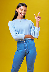 Image showing Pointing, happy and portrait of a woman in a studio for advertising, marketing or promotion. Smile, excited and young Indian female model with a direction hand gesture isolated by yellow background.