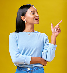 Image showing Pointing, smile and young woman in a studio for advertising, marketing or promotion. Happy, excited and Indian female model with a direction or arrow hand gesture isolated by yellow background.