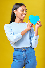 Image showing Donation, smile and woman with blue heart in studio for help, hope or empathy on yellow background. Charity, lady or social media poster for thank you, support for autism or people with a disability