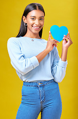 Image showing Portrait, smile and woman with blue heart in studio with help, hope or empathy on yellow background. Face, girl and social media icon for thank you, support and trust or people with loyalty to peace