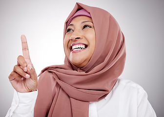 Image showing Muslim, thinking and a woman with an idea in studio for happiness, kindness and positive attitude. Hijab, islam and islamic fashion with a mature person on grey background pointing up at announcement
