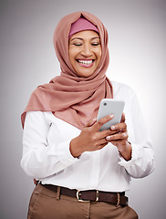 Image showing Smile, phone and mature muslim woman in a studio scroll on social media, mobile app or the internet. Happy, religion and islamic female model with a hijab browsing on a cellphone by a gray background