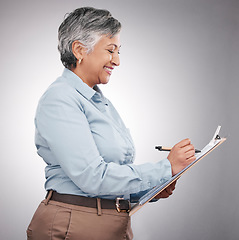 Image showing Clipboard, writing and senior woman in a studio planning, brainstorming or working on a schedule. Happy, smile and elderly female model with a paper list and pen isolated by a gray background.