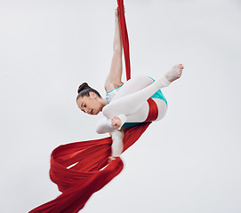 Image showing Acrobat, gymnastic and aerial silk with a woman in air for performance, sports and balance. Young athlete person or gymnast hanging on red fabric and white background with space, art and creativity