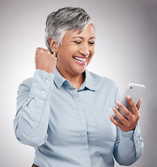 Image showing Celebration, phone and senior woman in studio winning an online bet, good news or prize. Happy, fist pump and elderly female model cheering with cellphone for success isolated by gray background.