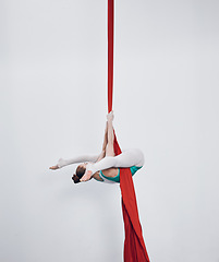 Image showing Gymnastics, acrobat and aerial silk with a woman in air for performance, sports and balance. Young athlete person or gymnast hanging on red fabric and white background with space, art and creativity