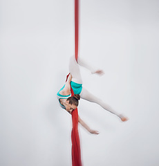 Image showing Gymnastics, acrobat and aerial silk with a sports woman in air for performance and balance. Young athlete person or gymnast hanging on red fabric and white background with space, art and creativity