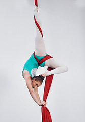 Image showing Gymnastics, aerial acrobat and silk with a woman in air for performance, sports and balance. Young athlete person or gymnast hanging on red fabric and white background with space, art and creativity