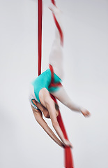 Image showing Sport, acrobat and aerial silk with a woman in air for performance, gymnastics and balance. Young athlete person or gymnast hanging on red fabric and white background with space, art and creativity