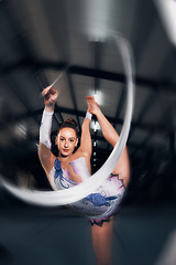 Image showing Woman, portrait and motion for ribbon gymnastics in competition, performance or concert in dark arena. Flexible dancer, athlete and balance of action, agile training and talent in solo rhythm contest