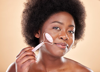 Image showing Black woman, face roller and portrait of beauty, rose quartz cosmetics and natural skincare on studio background. Happy model, facial massage and crystal tools for dermatology of lymphatic drainage
