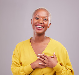 Image showing Grateful, smile and portrait of a black woman in a studio with sweet, happy and positive attitude. Empathy, gratitude and young African female model with thank you gesture isolated by gray background