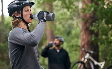 Image showing Forest, cyclist and men drinking water, exercise and tired with workout, refreshing and fitness. Healthy people, athlete and bikers in the woods, hydration and outdoor with liquid, bottles and helmet