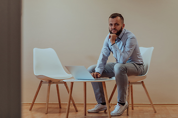 Image showing A confident businessman sitting and using laptop with a determined expression, while a beige background enhances the professional atmosphere, showcasing his productivity and expertise.