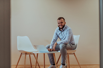 Image showing A confident businessman sitting and using laptop with a determined expression, while a beige background enhances the professional atmosphere, showcasing his productivity and expertise.