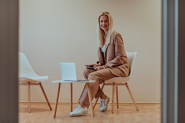 Image showing A professional businesswoman sits on a chair, surrounded by a serene beige background, diligently working on her laptop, showcasing dedication and focus in her pursuit of success