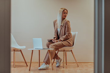 Image showing A professional businesswoman sits on a chair, surrounded by a serene beige background, diligently working on her laptop, showcasing dedication and focus in her pursuit of success