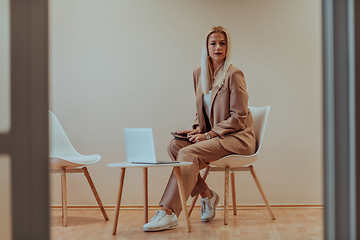 Image showing A professional businesswoman sits on a chair, surrounded by a serene beige background, diligently working on her laptop, showcasing dedication and focus in her pursuit of success