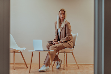 Image showing A professional businesswoman sits on a chair, surrounded by a serene beige background, diligently working on her laptop, showcasing dedication and focus in her pursuit of success