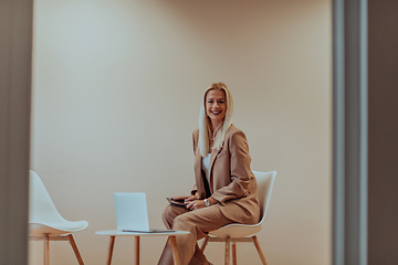 Image showing A professional businesswoman sits on a chair, surrounded by a serene beige background, diligently working on her laptop, showcasing dedication and focus in her pursuit of success