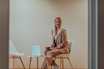 Image showing A professional businesswoman sits on a chair, surrounded by a serene beige background, diligently working on her laptop, showcasing dedication and focus in her pursuit of success