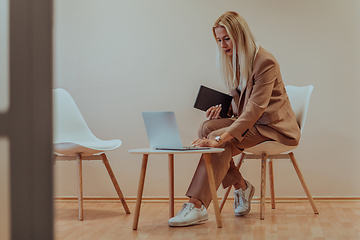 Image showing A professional businesswoman sits on a chair, surrounded by a serene beige background, diligently working on her laptop, showcasing dedication and focus in her pursuit of success