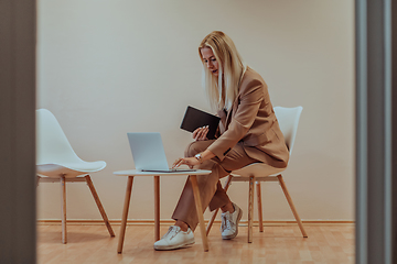 Image showing A professional businesswoman sits on a chair, surrounded by a serene beige background, diligently working on her laptop, showcasing dedication and focus in her pursuit of success