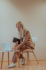 Image showing A professional businesswoman sits on a chair, surrounded by a serene beige background, diligently working on her laptop, showcasing dedication and focus in her pursuit of success