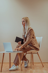 Image showing A professional businesswoman sits on a chair, surrounded by a serene beige background, diligently working on her laptop, showcasing dedication and focus in her pursuit of success