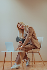 Image showing A professional businesswoman sits on a chair, surrounded by a serene beige background, diligently working on her laptop, showcasing dedication and focus in her pursuit of success