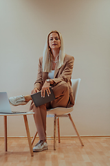 Image showing A professional businesswoman sits on a chair, surrounded by a serene beige background, diligently working on her laptop, showcasing dedication and focus in her pursuit of success