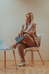 Image showing A professional businesswoman sits on a chair, surrounded by a serene beige background, diligently working on her laptop, showcasing dedication and focus in her pursuit of success