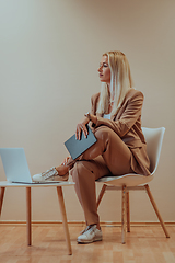 Image showing A professional businesswoman sits on a chair, surrounded by a serene beige background, diligently working on her laptop, showcasing dedication and focus in her pursuit of success