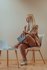 Image showing A professional businesswoman sits on a chair, surrounded by a serene beige background, diligently working on her laptop, showcasing dedication and focus in her pursuit of success