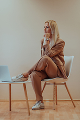 Image showing A professional businesswoman sits on a chair, surrounded by a serene beige background, diligently working on her laptop, showcasing dedication and focus in her pursuit of success