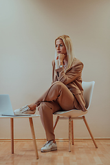 Image showing A professional businesswoman sits on a chair, surrounded by a serene beige background, diligently working on her laptop, showcasing dedication and focus in her pursuit of success